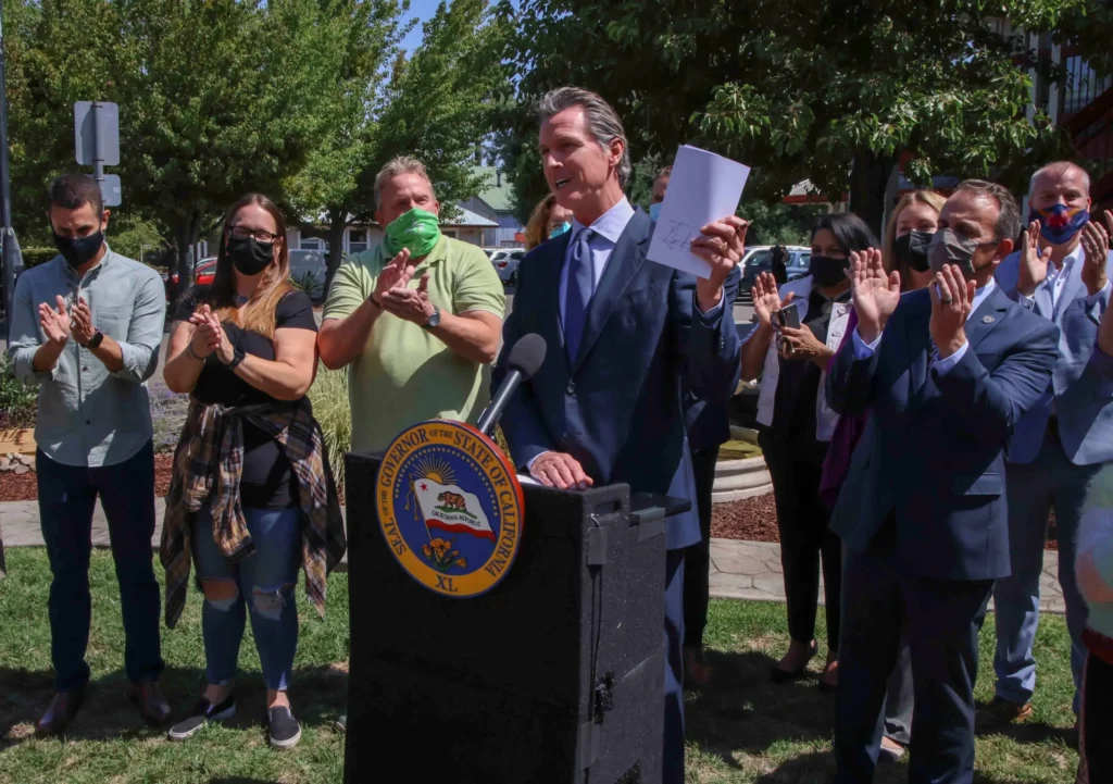 Photo of California governor Gavin Newsom speaking at a podium holding up a piece of paper
