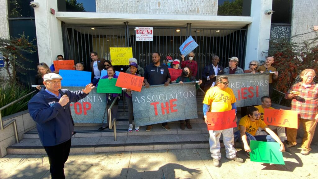Mike Bonin speaking in front of a crowd of people holding up posters that say Yes on U.L.A. and homes for homelessness